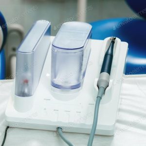 Dental equipment with a water unit and handpiece on a white surface.