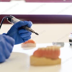 Dental technician using a handpiece tool with a dental model in the background.