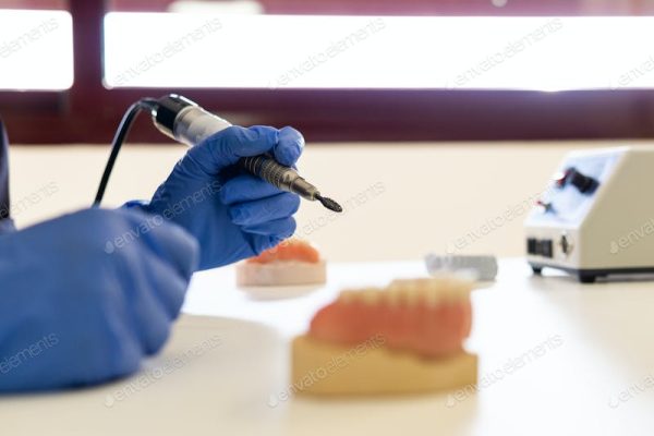 Dental technician using a handpiece tool with a dental model in the background.