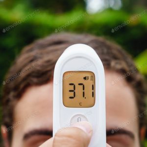 Person using a digital forehead thermometer showing 37.1°C.