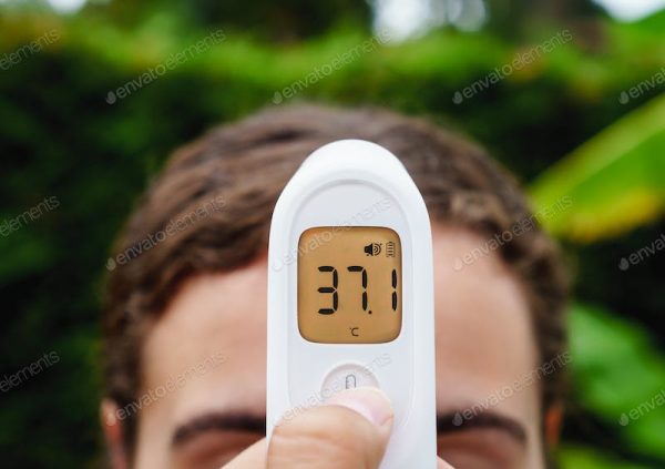 Person using a digital forehead thermometer showing 37.1°C.